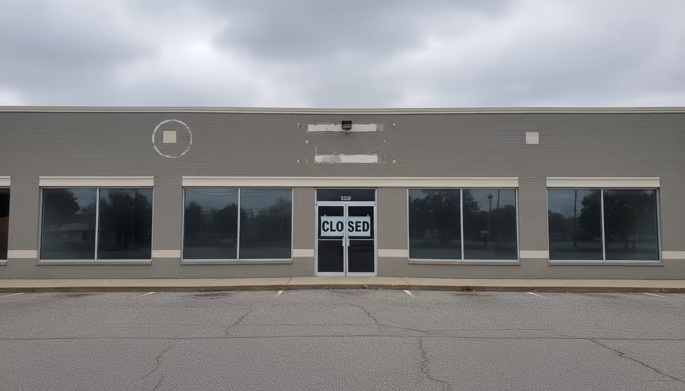 Closed commercial storefront with a CLOSED sign on the glass door and removed signage marks on the wall representing franchise termination