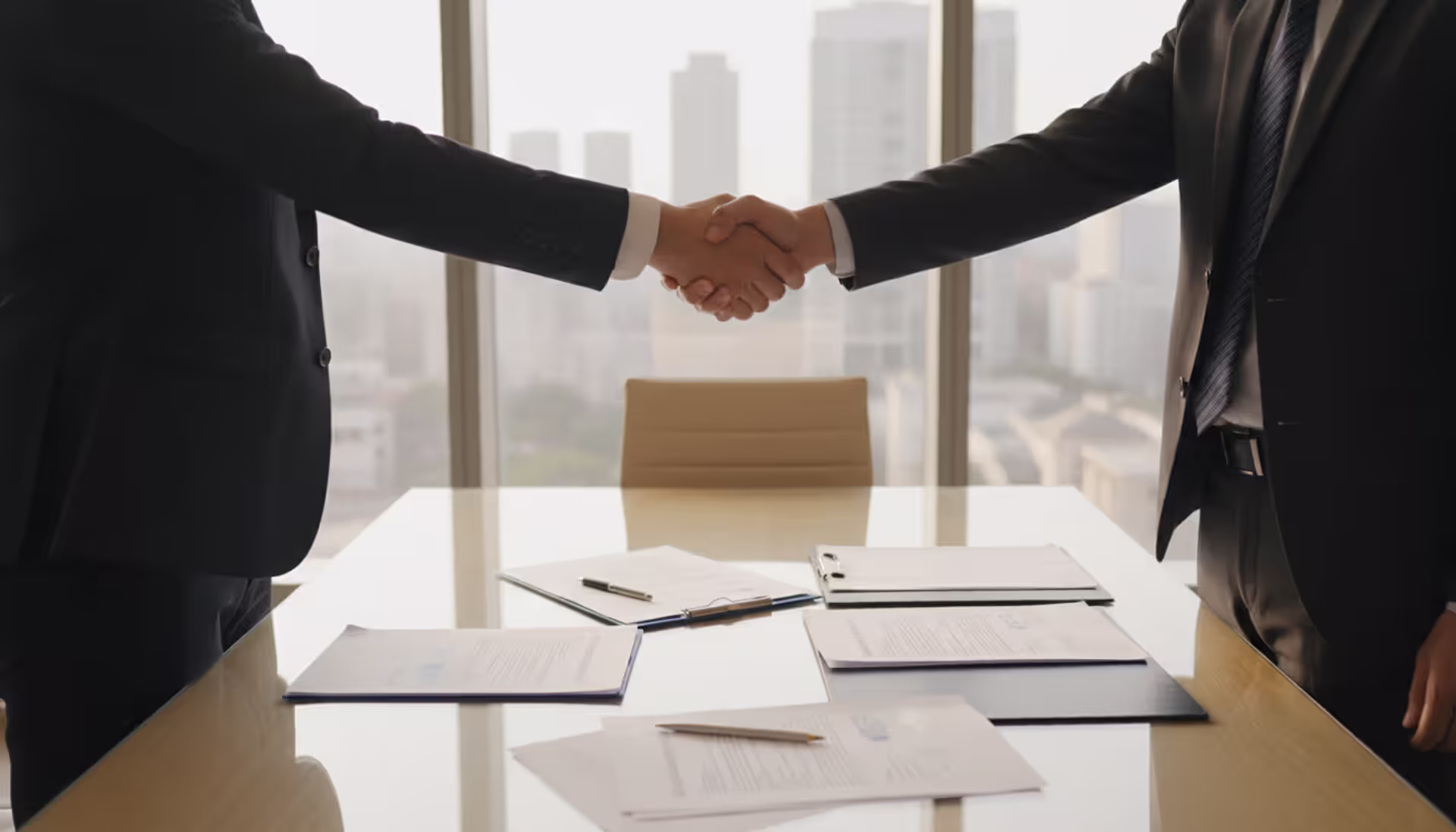 Two businessmen shaking hands in a modern office over documents symbolizing a transition services agreement in an M&A deal